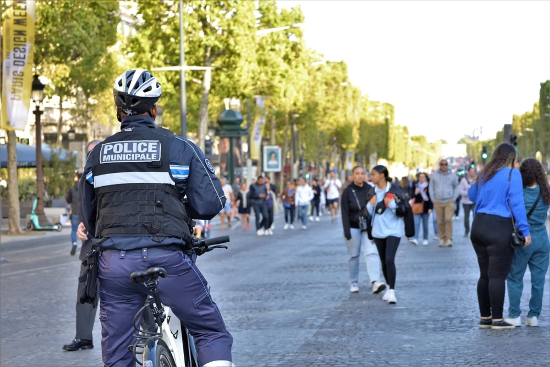 Policier municipal vu de dos à vélo, en patrouille sur une avenue parisienne
