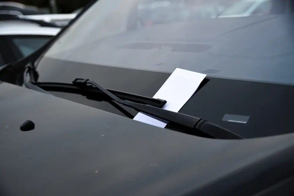 Contravention de stationnement glissée sous l'essuie-glace du pare-brise d'une voiture par un agent verbalisateur.
