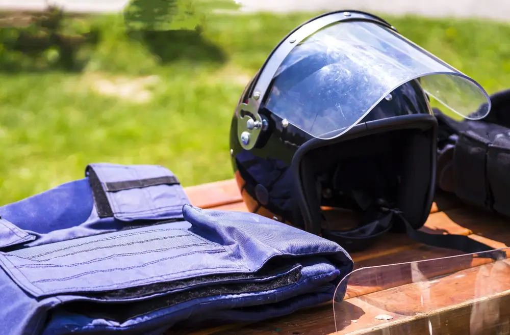 Équipement de police municipale avec casque à visière et gilet tactique posés sur une table en extérieur.