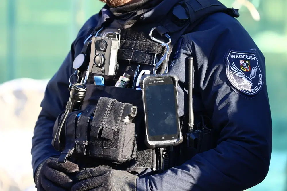 Caméra piéton et équipement professionnel fixés sur le gilet tactique d'un policier en uniforme.