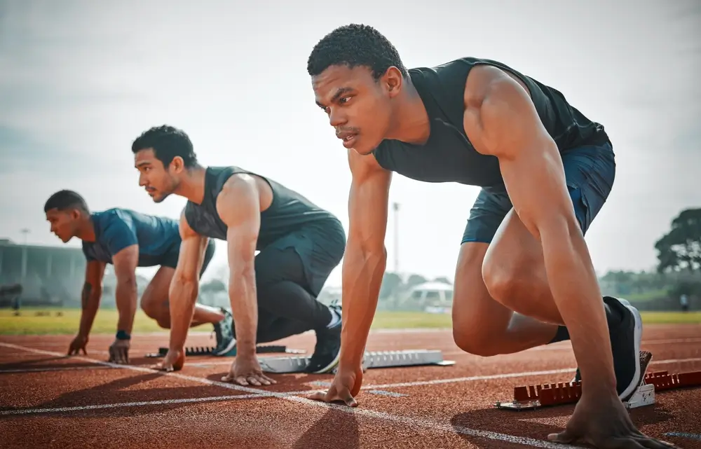 Trois candidats en position de départ sur une piste d'athlétisme pour une épreuve sportive de concours.